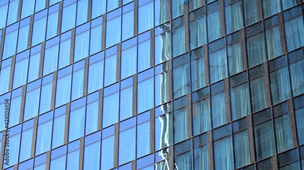 The glazed facade of an office building with reflected sky. Modern architecture buildings exterior background. Clouds sky reflection.