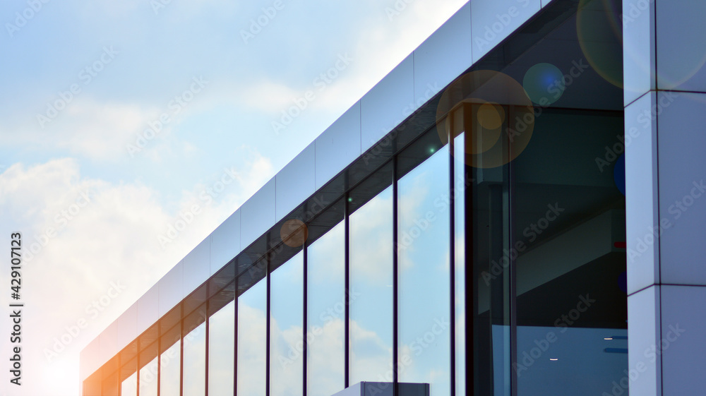 Fototapeta premium Blue sky reflection in glass facade of building. View of office building windows close up with sunrise, reflection and perspective.. Glass facade on a bright sunny day with sunbeams on the blue sky.