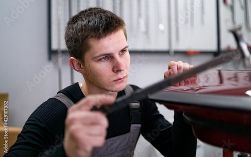 Processing of no paint using dent restoring technology by young technic looking narrowly on leveling surface while he punches it with rubber hammer. photo