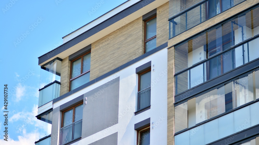 A fragment of modern architecture, walls and glass. Windows and balconies of a residential building against a blue sky. Detail of New luxury house and home complex. Part of city real estate property a A fragment of modern architecture, walls and glass. Windows and balconies of a residential building against a blue sky. Detail of New luxury house and home complex. Part of city real estate property a