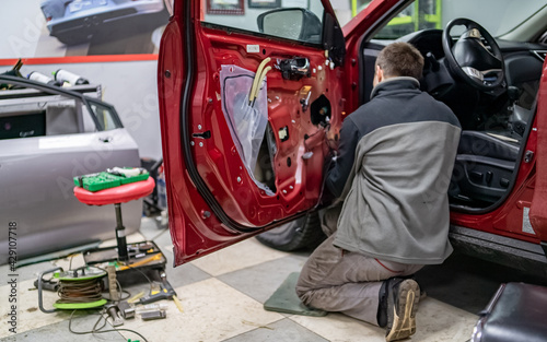 Mechanic guy in automobile service stay on a knees near car door at time of it dismantling to repair car after road accident