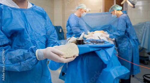 Surgeon in operation room is holding sterile breast silicone implant in hands.