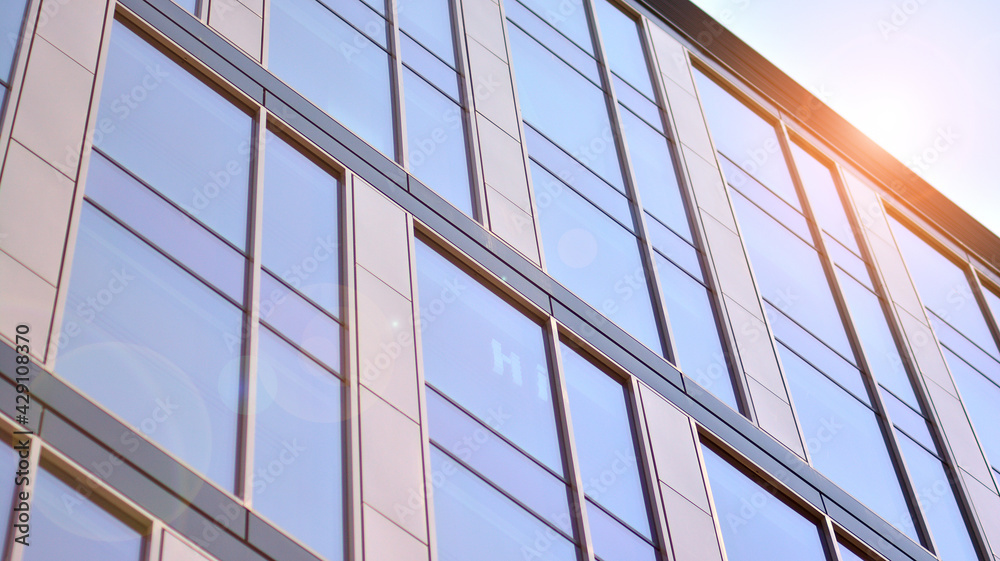 Blue sky reflection in glass facade of building. View of office building windows close up with sunrise, reflection and perspective.. Glass facade on a bright sunny day with sunbeams on the blue sky. Blue sky reflection in glass facade of building. View of office building windows close up with sunrise, reflection and perspective.. Glass facade on a bright sunny day with sunbeams on the blue sky.