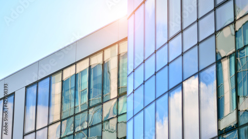 Blue sky reflection in glass facade of building. View of office building windows close up with sunrise  reflection and perspective.. Glass facade on a bright sunny day with sunbeams on the blue sky. 