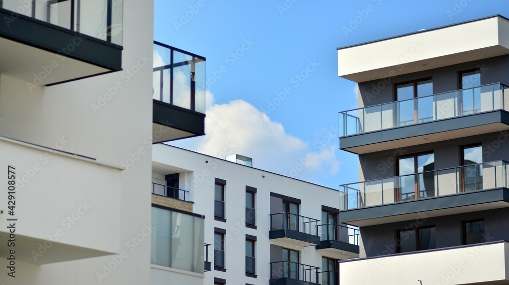 A fragment of modern architecture, walls and glass. Windows and balconies of a residential building against a blue sky. Detail of New luxury house and home complex. Part of city real estate property a A fragment of modern architecture, walls and glass. Windows and balconies of a residential building against a blue sky. Detail of New luxury house and home complex. Part of city real estate property a