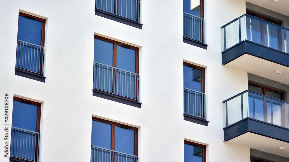 A fragment of modern architecture, walls and glass. Windows and balconies of a residential building against a blue sky. Detail of New luxury house and home complex. Part of city real estate property a