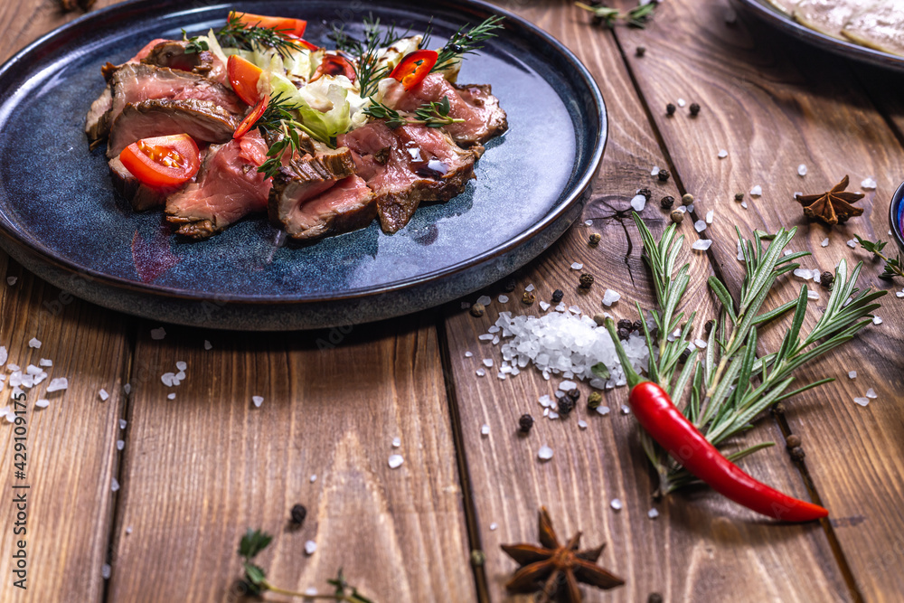 Beef tenderloin fried on fire with herbs, seasoned with spices, tomatoes. Wooden brown background decorated with rosemary, spices.