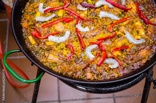 Close up of a tasty Spanish typical paella with prawns, peas, chicken and red pepper in a base of rice and vegetables. Traditional Spanish food. Paella cooked in a paellero. Paella ready to eat.