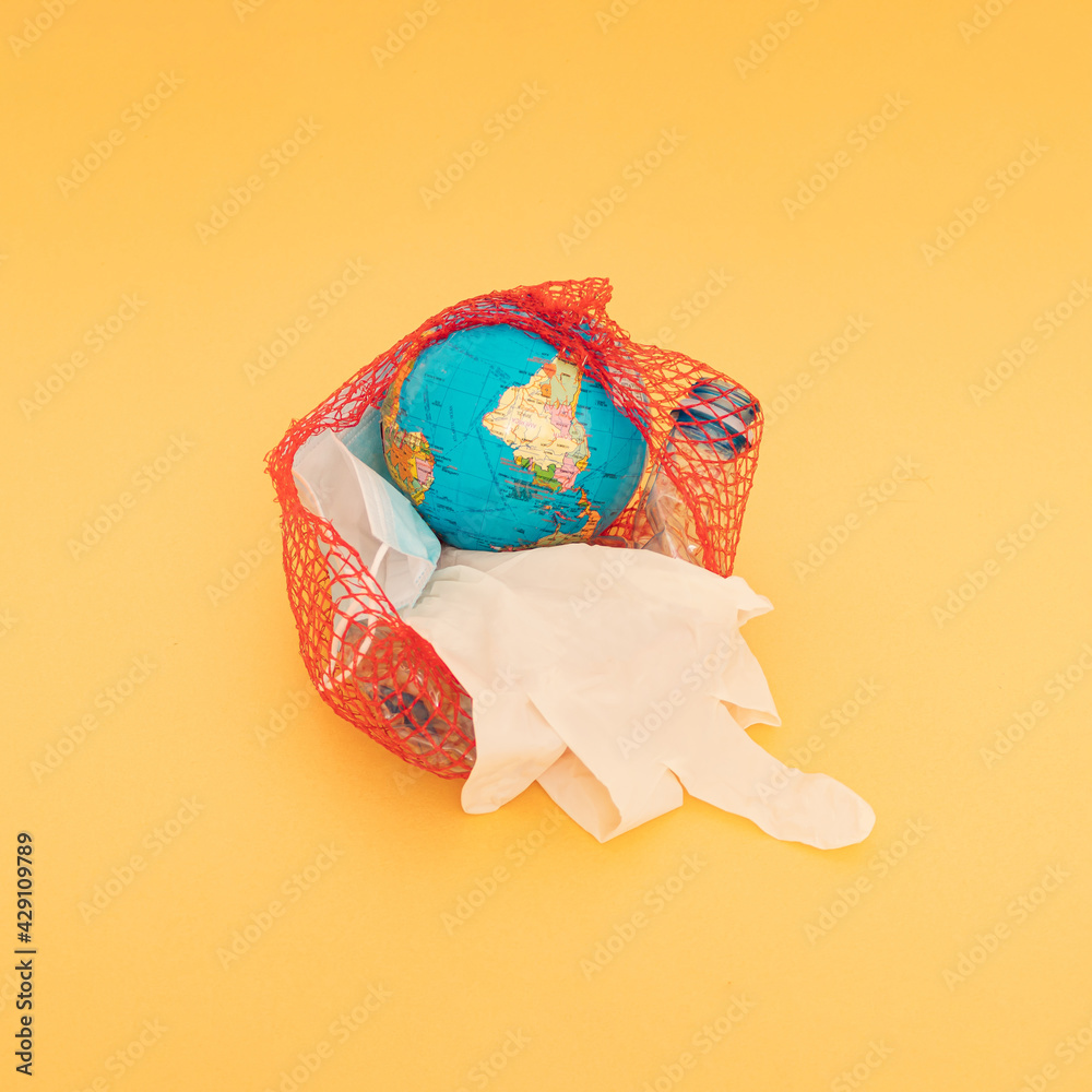 Globe, plastic bottle, blue surgical face mask and white glove in a nylon red bag. Golden background.