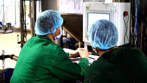 Two factory workers in protective suits sits near a screen of control panel and regulates a work of food factory machines photo