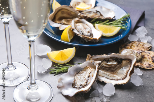 Fresh oysters with lemon, rosemary and glasses of champagne on grey table, closeup