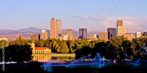 City Park Sprinklers - Sprinkers irrigate the lawn of City as a person walks along the City Park on at sunrise on a summer morning with the City Park Pavillion and skyline of downtown Denver, Colorado photo