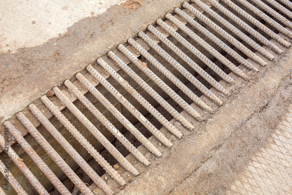drainage channel with a grate made of iron rods fittings dirty in clay, industrial wastewater infrastructure system close up. drainage channel with a grate made of iron rods fittings dirty in clay, industrial wastewater infrastructure system close up.
