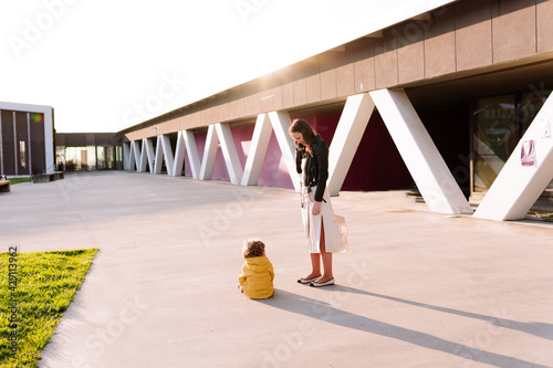 Beautiful young woman standing next to her son sitting angry on the ground at sunset. tantrum concept
