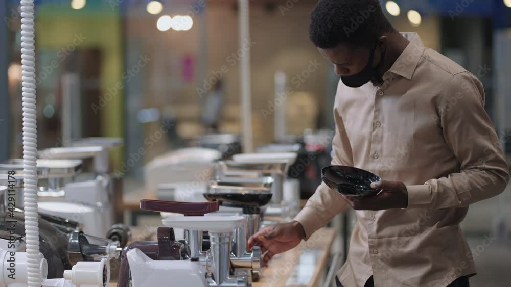 male shopper is choosing stand-alone meat grinder for home, viewing exhibition sample on shelf in store male shopper is choosing stand-alone meat grinder for home, viewing exhibition sample on shelf in store