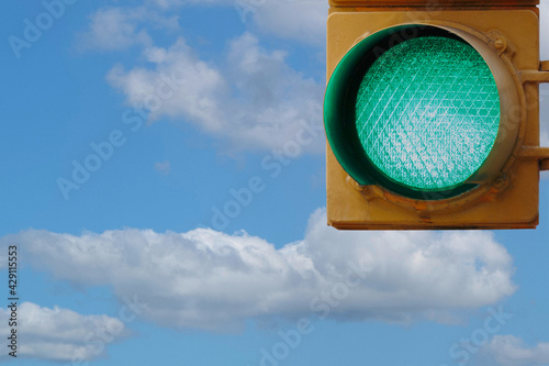 a green traffic light against a blue sky with fluffy white clouds with copy space, concept of a positive mindset, moving forward, permission to go, it's allowed, all systems go