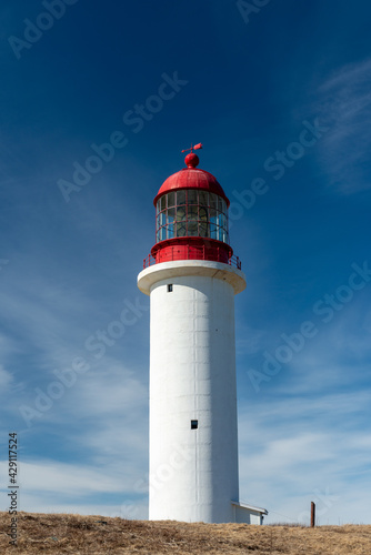 A vintage lighthouse tower with a round red metal roof.  In the center of the lighthouse is a vintage lamp made of multiple pieces of glass. On top of the white tower is a red metal wind arrow. © Dolores  Harvey