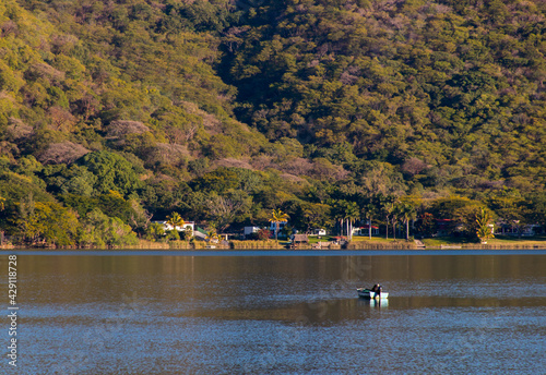 Small boat floating on the blue water of the crater lake of Santa Mar?a del Oro with green mountain side in background