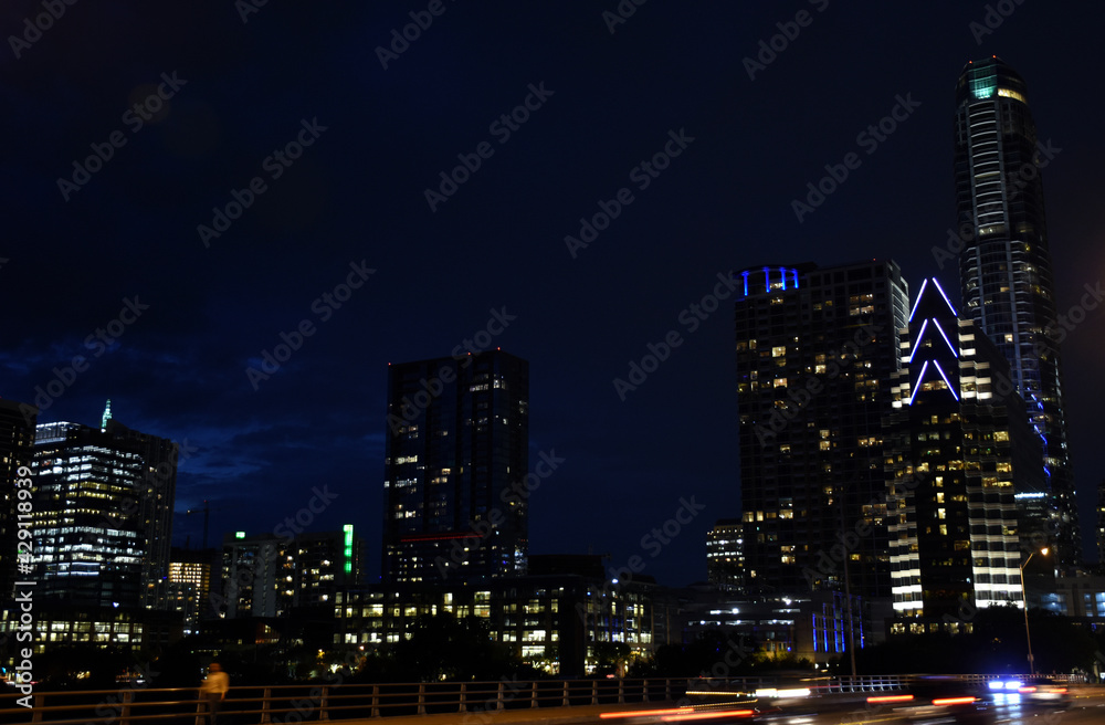 Fototapeta premium Night skyline over bridge with passing cars and lighted buildings