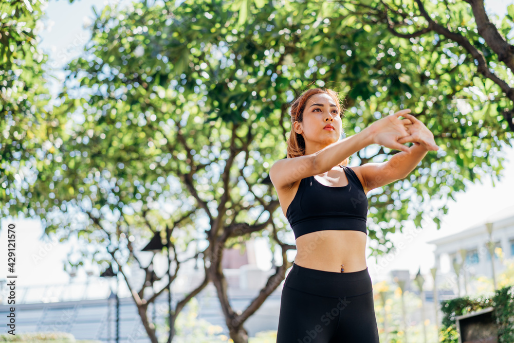 Young and fit Asian female runner in sportswear doing warmup exercise at the park by stretching arms outdoors before morning running and jogging Young and fit Asian female runner in sportswear doing warmup exercise at the park by stretching arms outdoors before morning running and jogging