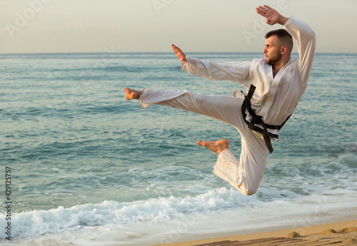 Cheerful man practising karate kata poses at seaside