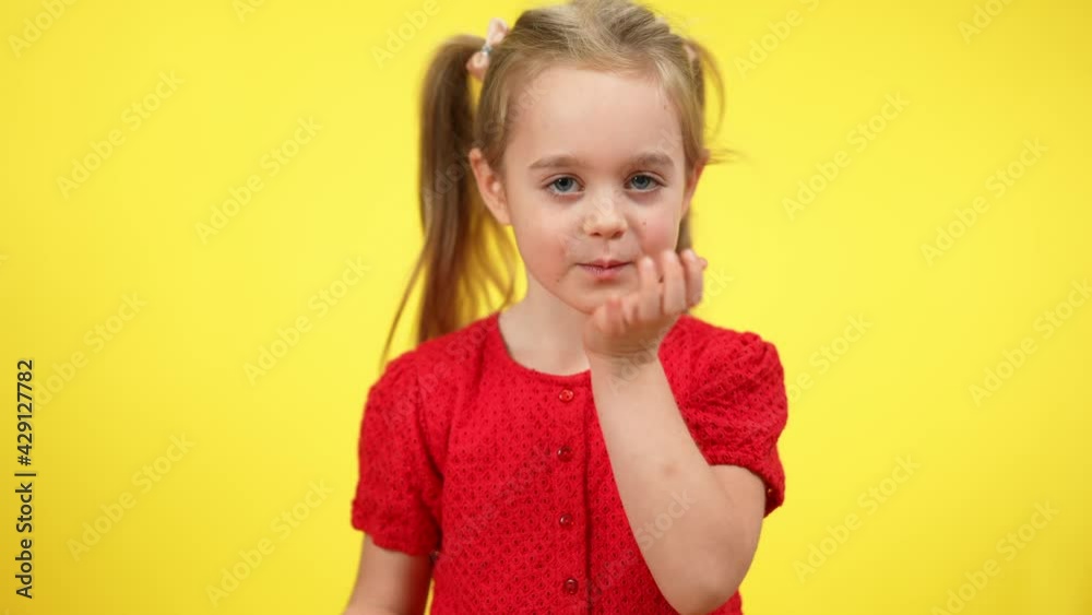 Middle shot of positive cute girl sending air kisses at yellow background. Pretty Caucasian child expressing good feelings at colored background Middle shot of positive cute girl sending air kisses at yellow background. Pretty Caucasian child expressing good feelings at colored background