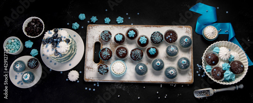Delicious cake and cupcakes in blue on dark background. Table setting for celebration. © bit24