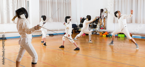 Portrait of young fencers with instructor engaged in fencing in training room