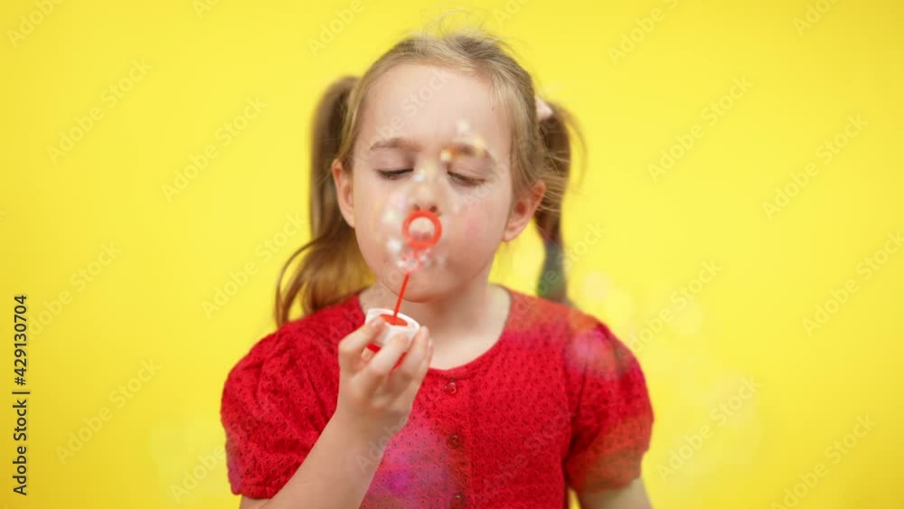 Portrait of blond cute girl with pigtails blowing soap bubbles at yellow background. Relaxed carefree Caucasian child having fun enjoying toy. Leisure and childhood happiness Portrait of blond cute girl with pigtails blowing soap bubbles at yellow background. Relaxed carefree Caucasian child having fun enjoying toy. Leisure and childhood happiness