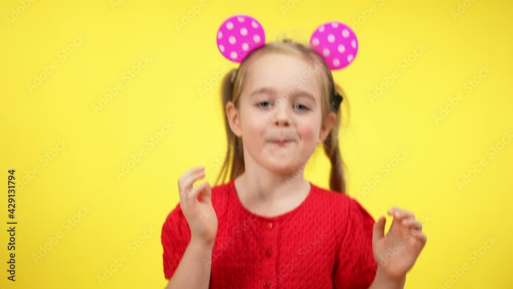 Joyful beautiful little girl with glowing toy mouse ears on head dancing at yellow background. Portrait of cheerful happy Caucasian child having fun. Happiness and leisure concept