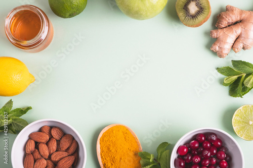 Healthy products for immunity boosting on green background. Fruits, honey, berries, ginger root, mint, nuts and turmeric. Health, virus prevention. Top view, flat lay, copy space, frame photo