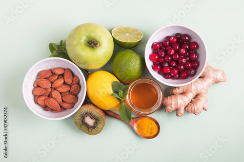 Healthy food for immunity boosting on green background. Lemon, honey, cranberry, ginger root, kiwi, apple, mint, nuts and turmeric. Health, products with vitamins, virus prevention. Top view, flat lay photo