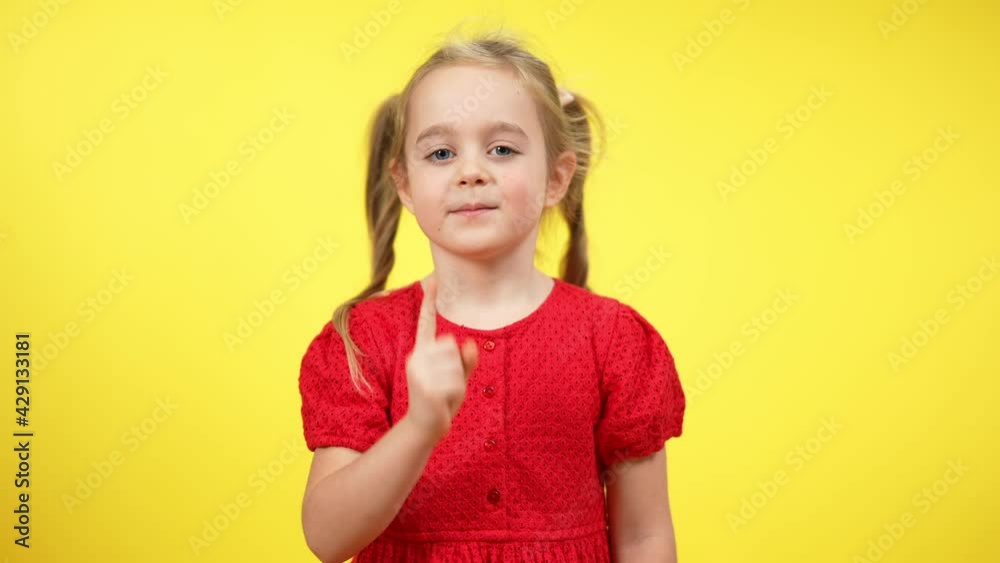 Middle shot of cute charming little girl shaking finger in slow motion disapproving. Portrait of beautiful confident Caucasian kid posing at yellow background Middle shot of cute charming little girl shaking finger in slow motion disapproving. Portrait of beautiful confident Caucasian kid posing at yellow background