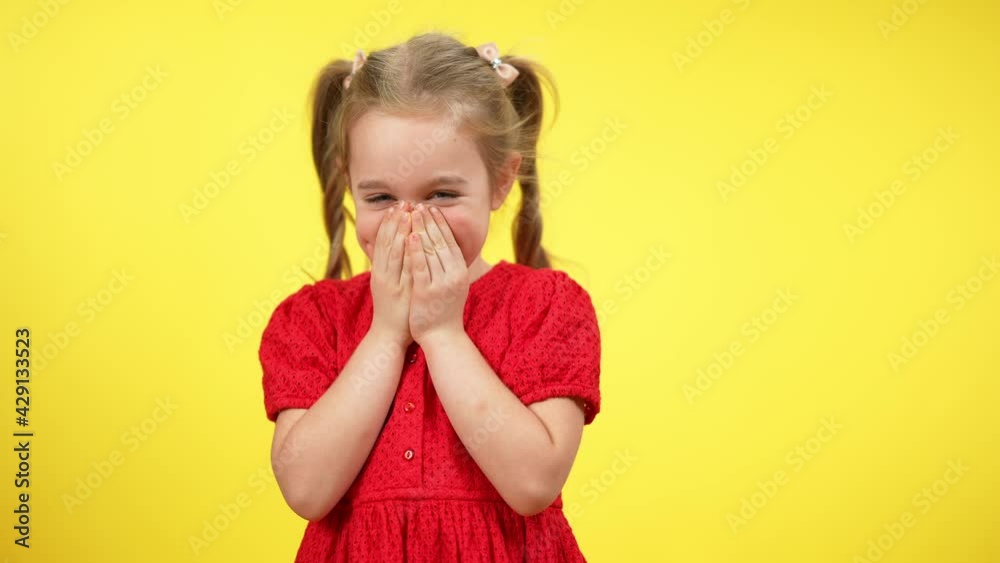 Funny cute little shy girl laughing closing mouth with hands. Portrait of beautiful blond Caucasian child with grey eyes posing at yellow background having fun Funny cute little shy girl laughing closing mouth with hands. Portrait of beautiful blond Caucasian child with grey eyes posing at yellow background having fun