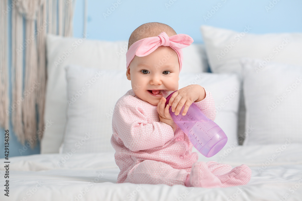 Cute little baby drinking water from bottle on bed in room Cute little baby drinking water from bottle on bed in room