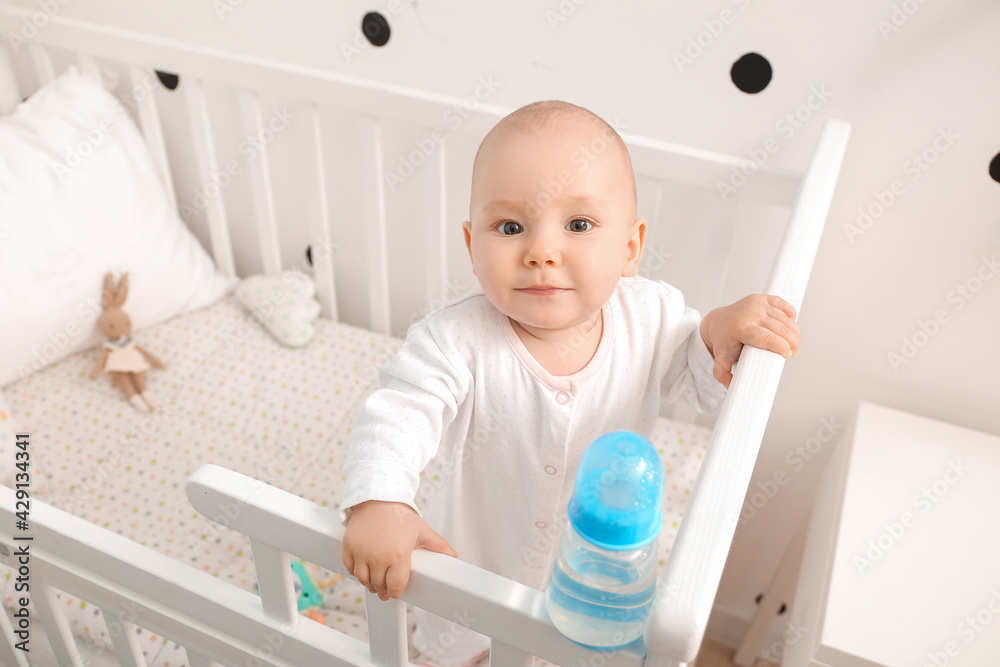 Cute little baby with bottle of water in crib at home Cute little baby with bottle of water in crib at home