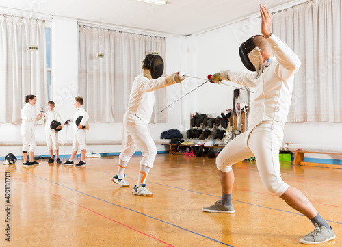 Serious group practicing effective fencing techniques in sparring in training room © JackF