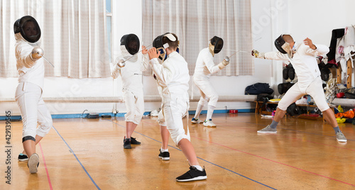 Portrait of young fencers with instructor engaged in fencing in gym