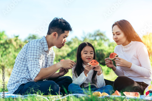 happy Asian family is having picnic in garden and eating water melon with their daughters on holiday happily. © jumlongch