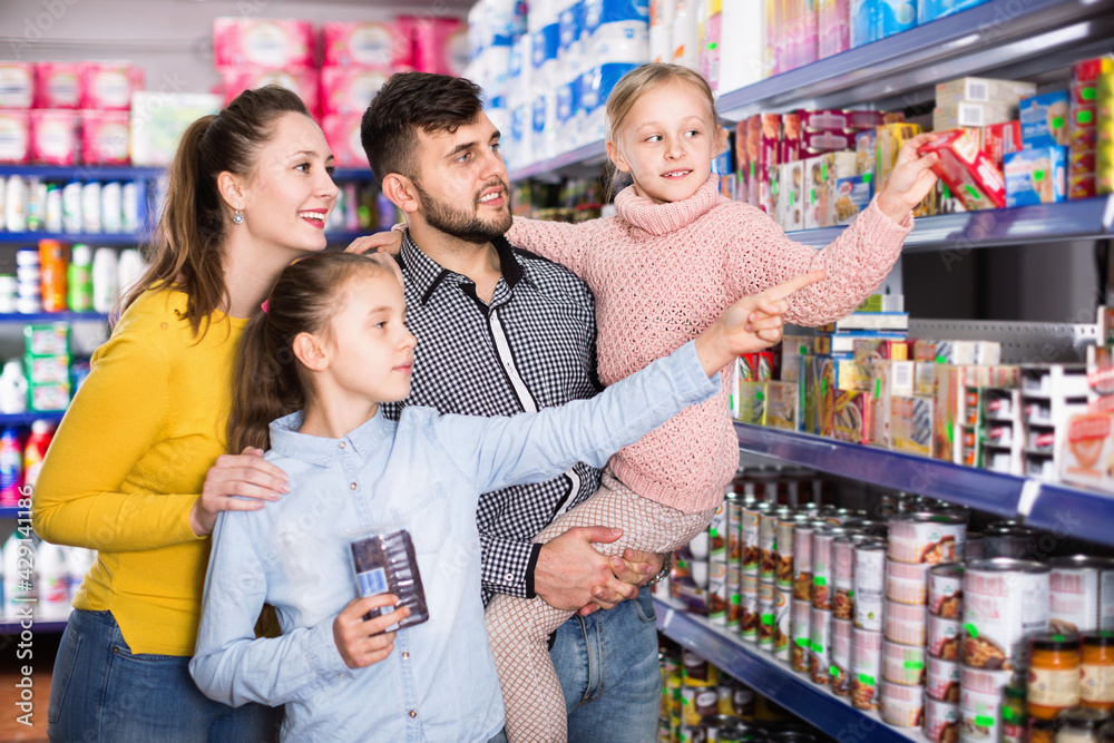 Happy cheerful smiling family with two little girls buying food products in supermarket