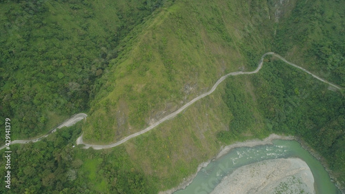 Aerial view of mountain river in the cordillera, road on the slopes, mountains covered forest, trees. Cordillera region. Luzon, Philippines. Mountain landscape in cloudy weather. © Alex Traveler