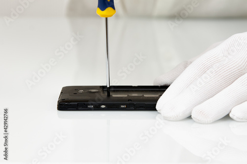 A white-gloved hand uses a screwdriver to disassemble the phone. Smartphone repair process