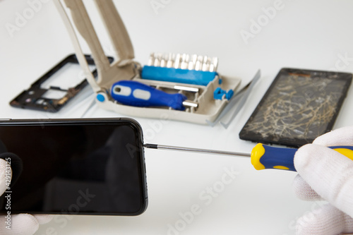 Disassembled smartphone and tools for its repair: tweezers and screwdrivers. The process describing the repair of a smartphone