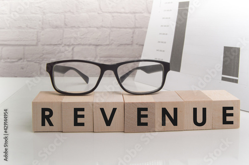 Word Revenue on ascending arrow above bar graph of Wooden small cubes isolated on black background. Chalk drawing on blackboard. Business Concept image.