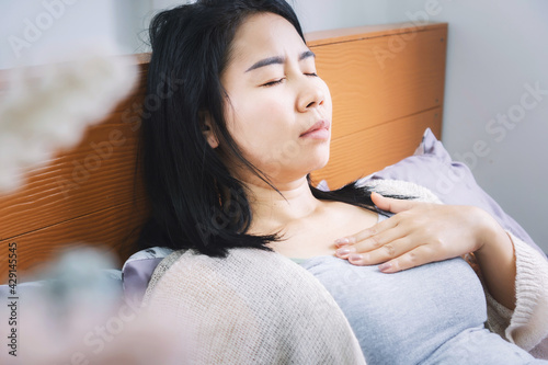 Asian woman laydown in bed having problem with heartburn from acid reflux difficult to breathe after wakeup in morning photo