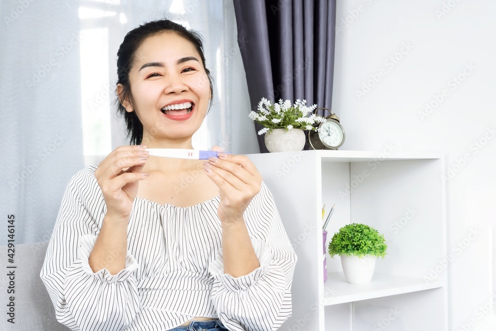 excited Asian woman smiling and laughing with happy face showing positive result of pregnancy test in hand excited Asian woman smiling and laughing with happy face showing positive result of pregnancy test in hand
