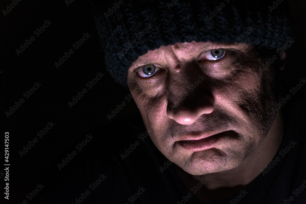 A brutal portrait of a man on a black background in a knitted hat, blurred. Strong-willed male gaze. The eyes of a man. A brutal portrait of a man on a black background in a knitted hat, blurred. Strong-willed male gaze. The eyes of a man.