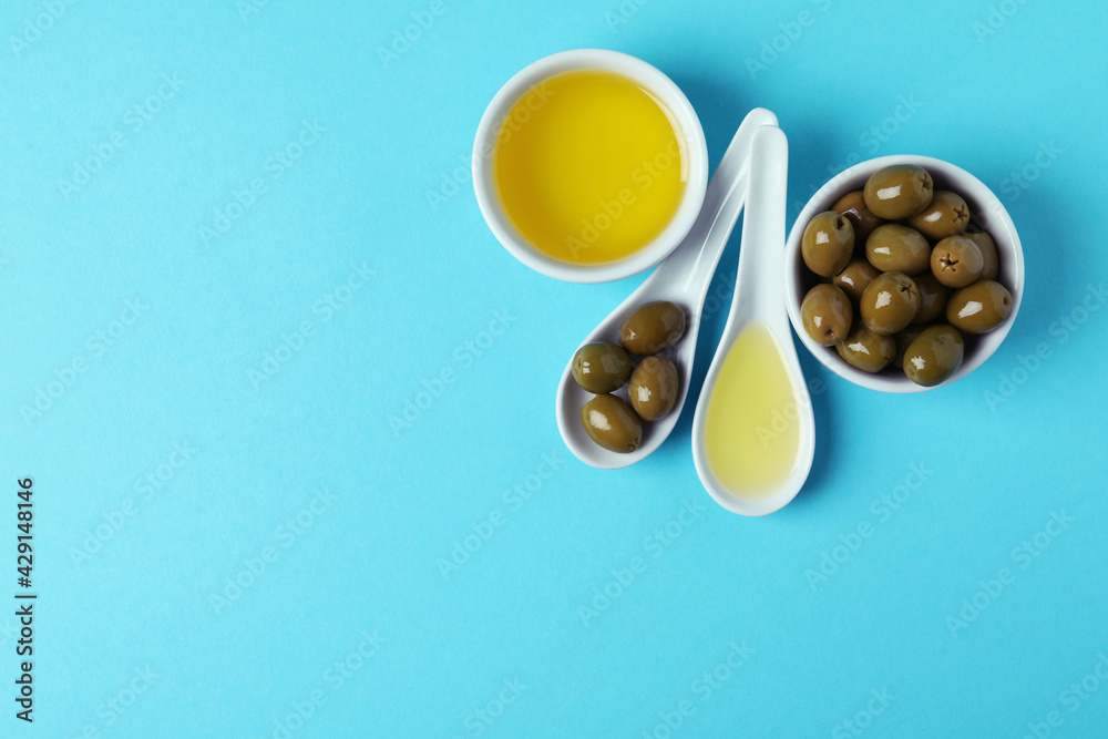 Spoons and bowls with olives and oil on blue background