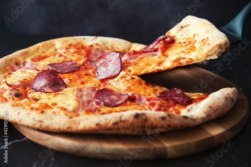 Delicious homemade pizza on a wooden plate against the black background