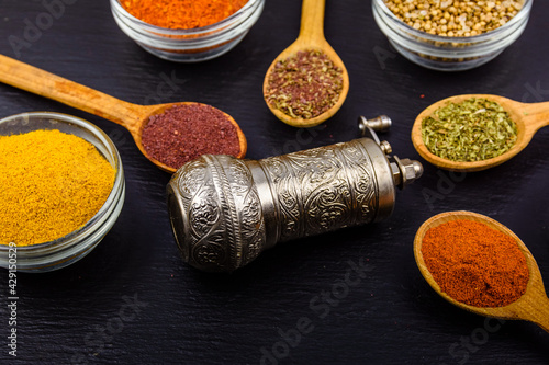 Spoons and bowls with oriental spices and spice mill on a slate board